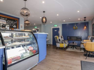 A cafe interior with a display case of cakes and pastries a blue counter and seating area with chairs and tables at Number 1 Dome in Derrybeg County Donegal