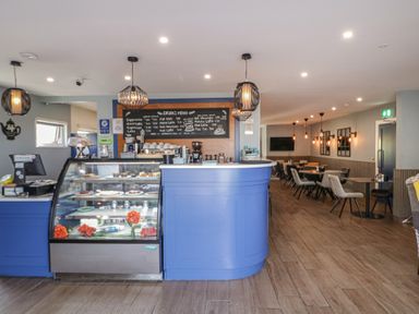 A cafe interior with a blue counter and glass display case with cakes and a menu on the wall at Number 1 Dome in Derrybeg County Donegal