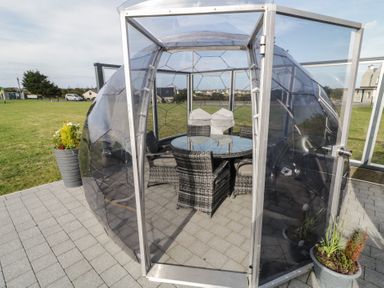 An outdoor seating area with a round glass table and wicker chairs inside a transparent dome at Number 1 Dome in Derrybeg County Donegal