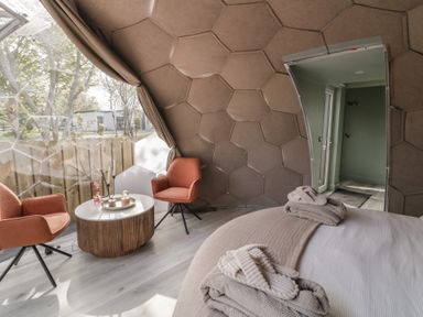 A room with two orange chairs and a round wooden table near a window in a dome-shaped structure with a bed and towels at Number 2 Dome in Derrybeg County Donegal