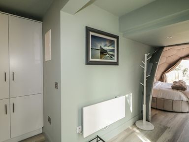 A bedroom with a bed visible through a hexagonal frame a coat stand a heating unit a framed picture and white cupboards at Number 2 Dome in Derrybeg County Donegal