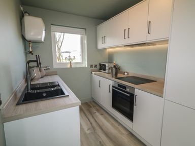 A narrow kitchen with a sink and cabinets under a window and a stove oven with overhead cupboards at Number 2 Dome in Derrybeg County Donegal