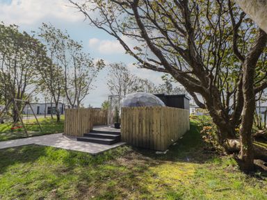 A fenced wooden deck with an entrance and steps leading to a clear geodesic dome in a grassy outdoor area with trees at Number 2 Dome in Derrybeg County Donegal