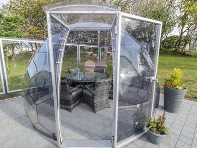 A transparent dome structure with a glass table and chairs inside on a paved patio at Number 2 Dome in Derrybeg County Donegal