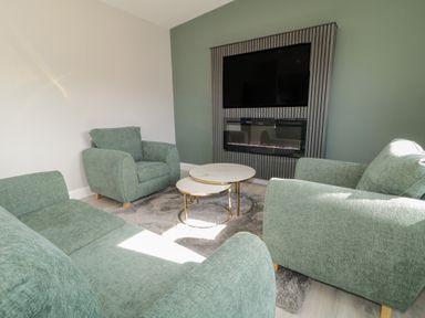 A sitting room with green upholstered chairs sofas a rug coffee tables a mounted television and fireplace at Number 2 Villa - The View in Derrybeg County Donegal