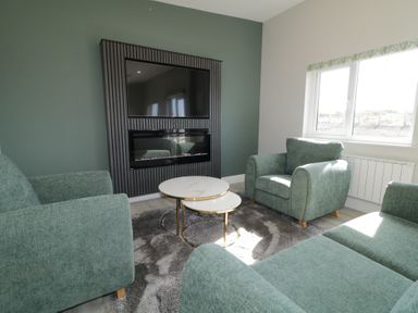 A living room with green sofas coffee tables and a wall-mounted tv at Number 2 Villa - The View in Derrybeg County Donegal