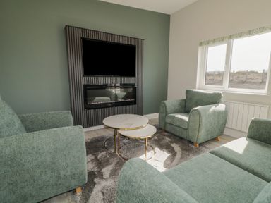 A living room with green armchairs a round coffee table a gray rug a mounted television and a window at Number 2 Villa - The View in Derrybeg County Donegal