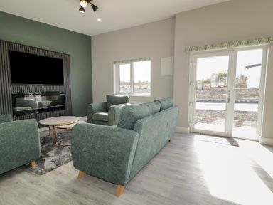 A living room with green sofas a wall-mounted TV and fireplace next to windows and glass doors at Number 2 Villa - The View in Derrybeg County Donegal