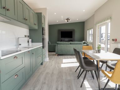 A kitchen with green cabinets and a dining table with chairs next to a living room with sofas and a wall-mounted tv at Number 2 Villa - The View in Derrybeg County Donegal