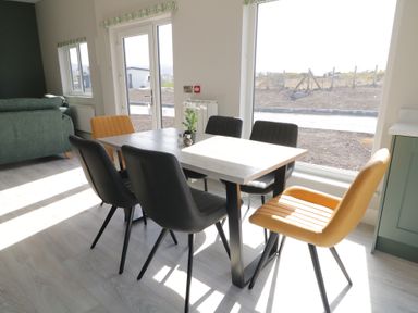 A dining area with a table surrounded by six chairs and a sofa near windows at Number 2 Villa - The View in Derrybeg County Donegal