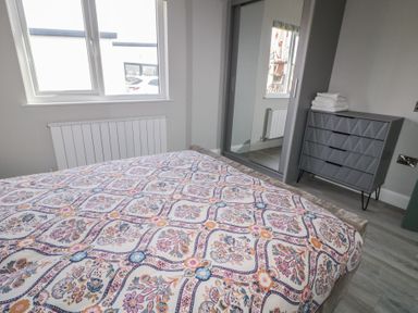 A bedroom with a patterned bedspread a window a radiator a mirrored wardrobe and a chest of drawers at Number 2 Villa - The View in Derrybeg County Donegal