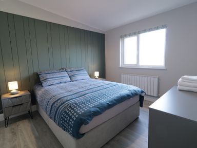 A bedroom with a bed two bedside tables with lamps a window and a dresser with towels at Number 2 Villa - The View in Derrybeg County Donegal