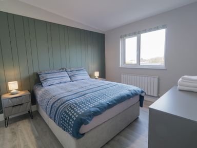 A bedroom with a double bed blue patterned bedding bedside tables with lamps and a window at Number 2 Villa - The View in Derrybeg County Donegal