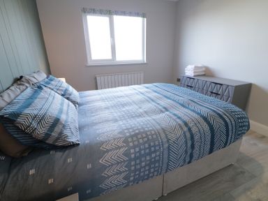 A bedroom with a bed with patterned blue and white bedding a window and a dresser with folded towels at Number 2 Villa - The View in Derrybeg County Donegal