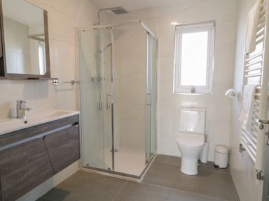 A bathroom with a glass shower enclosure a sink with a mirror a toilet and a window at Number 2 Villa - The View in Derrybeg County Donegal