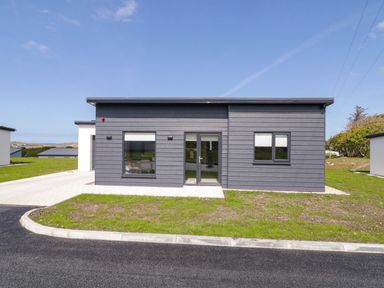 A modern single story house with grey cladding windows and a door surrounded by grass and paved driveway at Number 2 Villa - The View in Derrybeg County Donegal