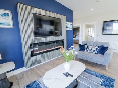 A living room with a grey sofa a white marble coffee table with a vase of flowers a wall mounted television above a modern fireplace at Number 5 Villa - The View in Derrybeg County Donegal