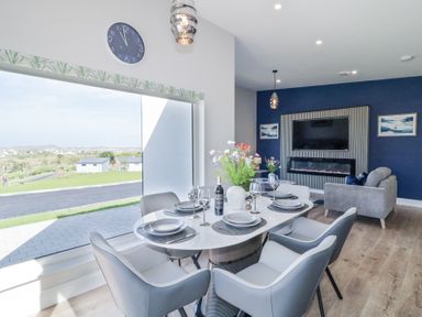 A dining area with a table set for six and a living room with a large television and fireplace at Number 5 Villa - The View in Derrybeg County Donegal