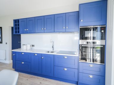 A kitchen with blue cabinets white countertop built in oven and microwave at Number 5 Villa - The View in Derrybeg County Donegal