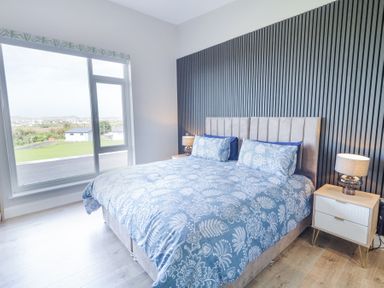 A bedroom with a large bed blue floral bedding two bedside tables with lamps and a window showing outside view at Number 5 Villa - The View in Derrybeg County Donegal