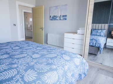 A bedroom with a blue patterned bedspread a dresser with towels and a mirrored wardrobe at Number 5 Villa - The View in Derrybeg County Donegal