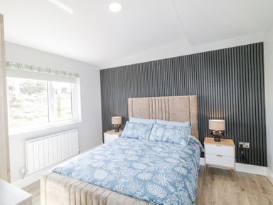 A bedroom with a bed with blue floral bedding two bedside tables with lamps and a window at Number 5 Villa - The View in Derrybeg County Donegal