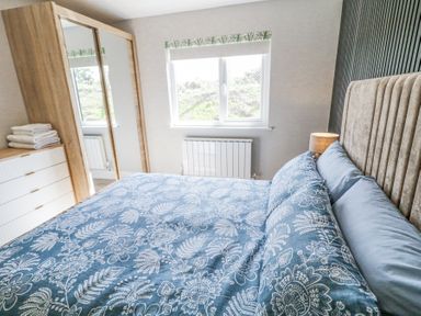A bedroom with a bed with blue floral bedding a wooden wardrobe with mirrored doors a chest of drawers and a window at Number 5 Villa - The View in Derrybeg County Donegal
