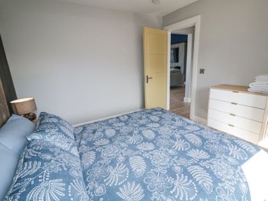 A bedroom with a double bed covered in blue floral bedding next to a wooden dresser with folded towels at Number 5 Villa - The View in Derrybeg County Donegal