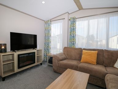 A living room with a brown sofa yellow pillow TV on wooden cabinet and floral curtains at HW42 in Bognor Regis