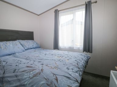 A bedroom with a bed covered in floral patterned bedding and a window with gray curtains at HW42 in Bognor Regis