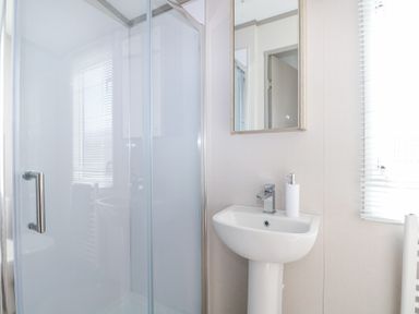 A bathroom with a shower enclosure a pedestal sink with a soap dispenser and a mirror cabinet at HW42 in Bognor Regis