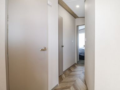 A hallway with two closed doors and one open door showing a bedroom at HW42 in Bognor Regis