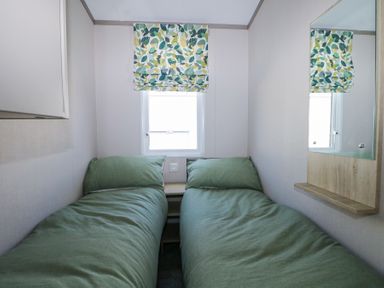 A small bedroom with two single beds with green bedding a window with leaf patterned blinds and a wall mirror at HW42 in Bognor Regis