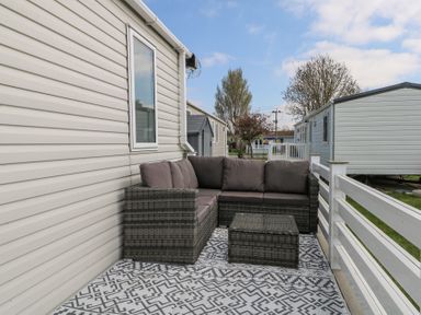 An outdoor patio area with a wicker sofa set and patterned rug beside mobile homes at HW42 in Bognor Regis