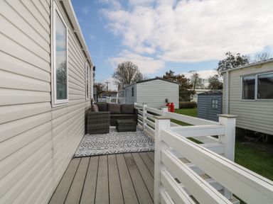 An outdoor deck with a gray sofa set and patterned rug near mobile homes at HW42 in Bognor Regis