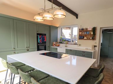A kitchen with a central island and green cabinets at Yew Tree Cottage Mealsgate near Ireby