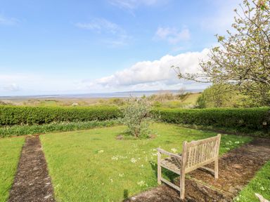 A garden with a wooden bench a small tree and a hedge overlooking a distant landscape at Burry House in Llanmorlais