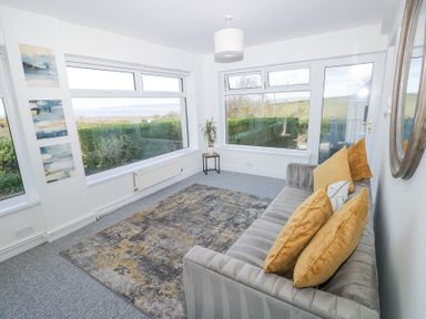 A sitting room with a gray sofa with yellow cushions a patterned rug and large windows showing a garden at Burry House in Llanmorlais
