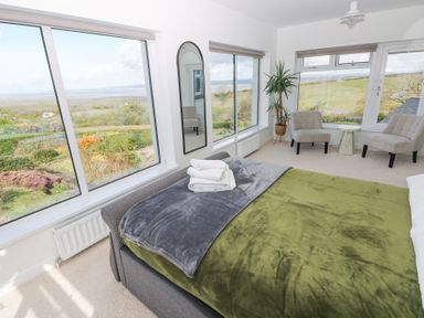 A bedroom with a bed near corner windows and two chairs around a small table at Burry House in Llanmorlais