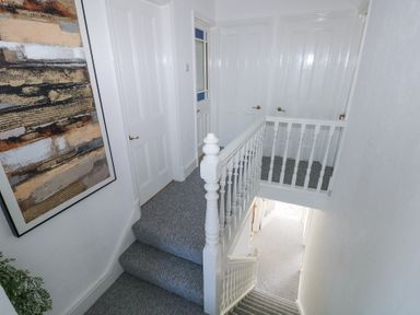 A staircase with white railings and gray carpet leading to a hallway with white doors and a framed abstract wall art at Burry House Llanmorlais