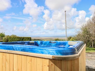 An outdoor blue hot tub with a wooden exterior with a scenic view of fields and sky at Burry House in Llanmorlais