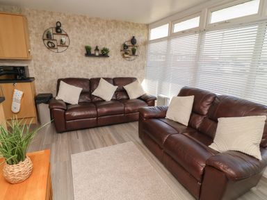A living room with two brown leather sofas with white cushions and wall shelves with plants at 56 Cherry Park Chalet in Chapel St Leonards