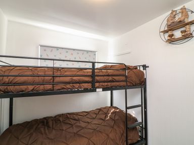 A bedroom with a black metal bunk bed and brown bedding with a window and bird patterned blind at 56 Cherry Park Chalet in Chapel St Leonards