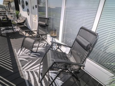A balcony with black reclining chairs and a small table on a patterned rug at 56 Cherry Park Chalet in Chapel St Leonards