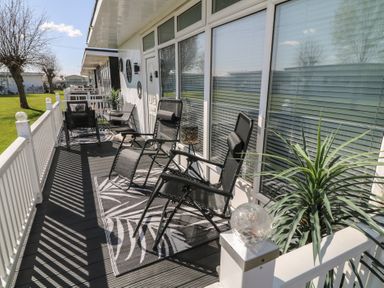 A porch with reclining chairs a small table and plants at 56 Cherry Park Chalet in Chapel St Leonards