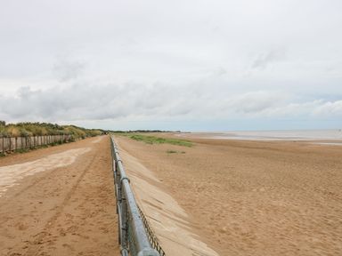 A sandy beach with a metal railing and a path alongside vegetation at 56 Cherry Park Chalet in Chapel St Leonards