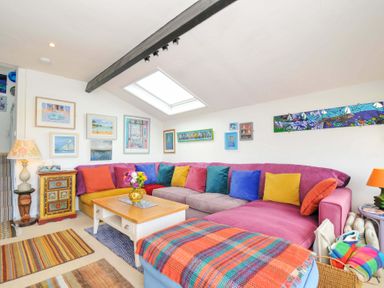 A living room with a large sectional sofa with colorful cushions and a wooden coffee table under a skylight at 5 Esplanade in Fowey