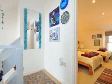 A hallway with a mirror and wall decorations leading to a bedroom with two single beds with towels on them at 5 Esplanade in Fowey