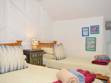 A bedroom with two single beds, a painted nightstand with a lamp, and framed pictures on the wall at 5 Esplanade in Fowey