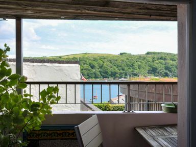 A balcony with a wooden table and greenery overlooking a river with boats and hills in the background at 5 Esplanade in Fowey